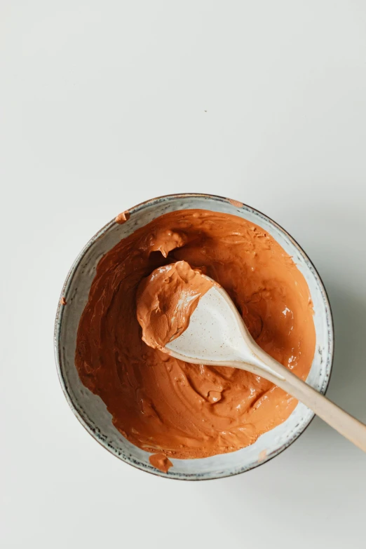 a close up of a bowl of food with a wooden spoon, a gouache, by Nina Hamnett, process art, chocolate frosting, terracotta, hegre, thumbnail