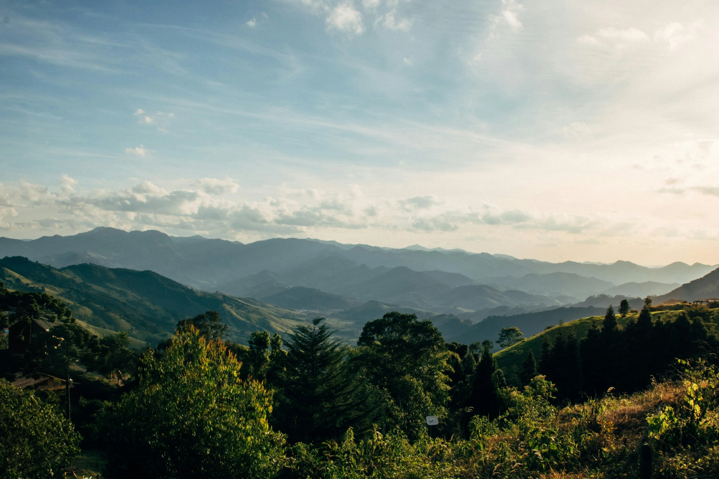 a view of the mountains from the top of a hill, by Lee Loughridge, unsplash contest winner, sumatraism, sunny day time, lush countryside, late afternoon, wide high angle view