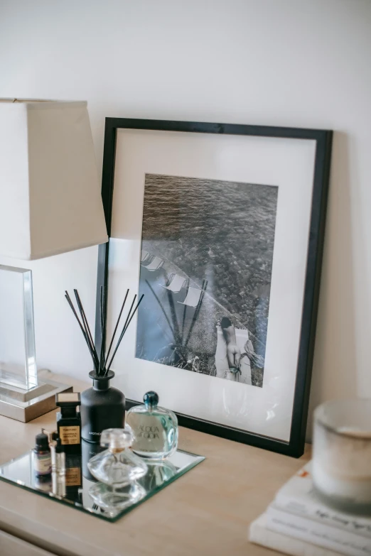 a table topped with a lamp next to a picture, by Richmond Barthé, unsplash, visual art, bedroom, charcoal and champagne, jar on a shelf, seaside