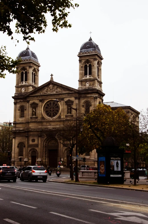 a group of cars driving down a street next to a church, romanesque, parisian buildings, front facing, building facing