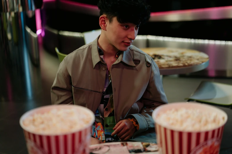 a man sitting at a table with two cups of popcorn, an album cover, pexels, hyperrealism, cai xukun, sitting in a movie theater, cinematic outfit photo, eating chips and watching tv