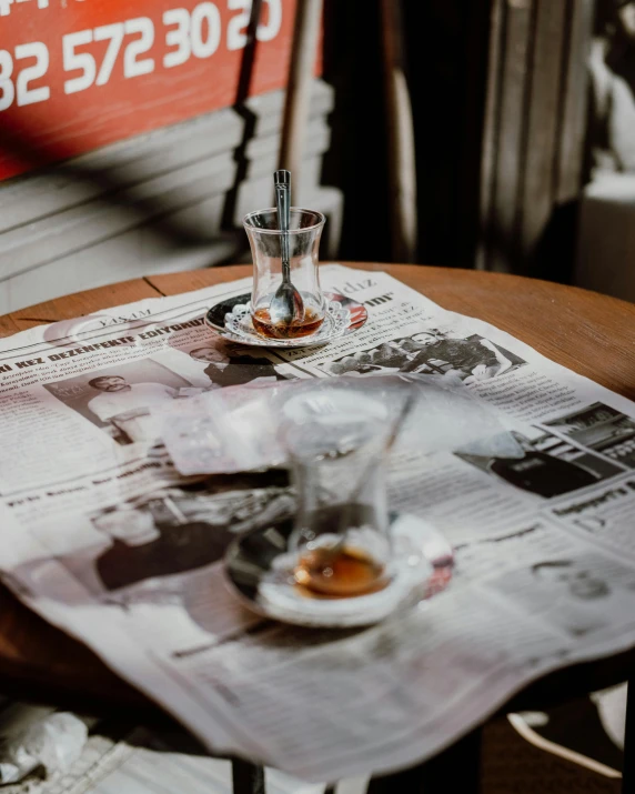 a newspaper sitting on top of a wooden table, two cups of coffee, whiskey, nika maisuradze, thumbnail