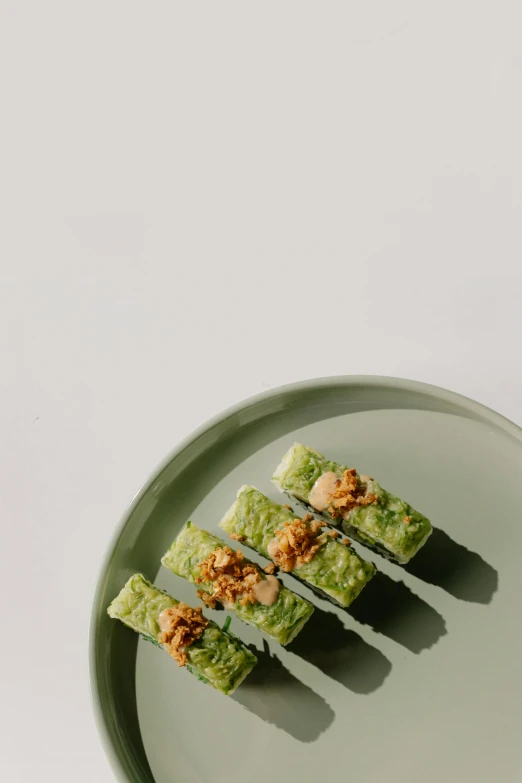 a plate with four pieces of sushi on it, inspired by Nishida Shun'ei, unsplash, conceptual art, muted green, wide long view, indonesia, from side