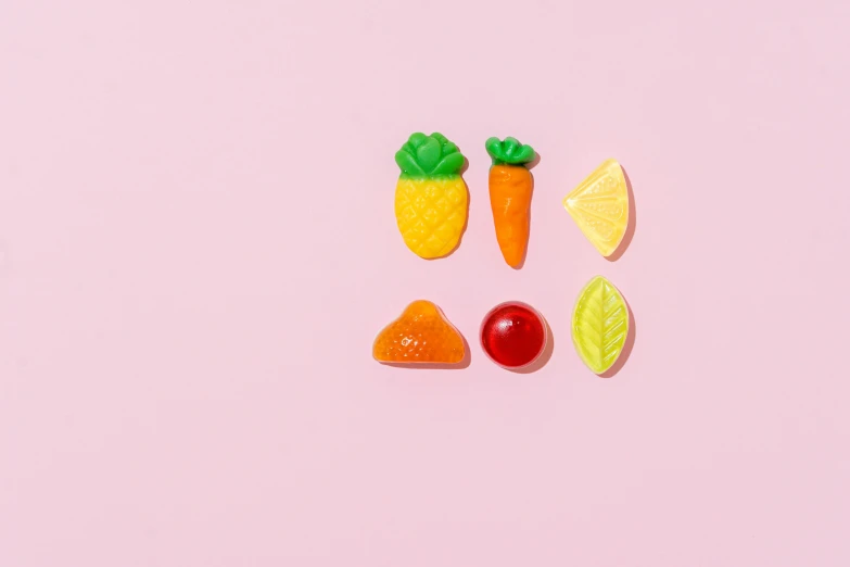 a close up of fruit and vegetables on a pink surface, by Julia Pishtar, plasticien, gummy candies, 6 pack, detailed product image, carrot