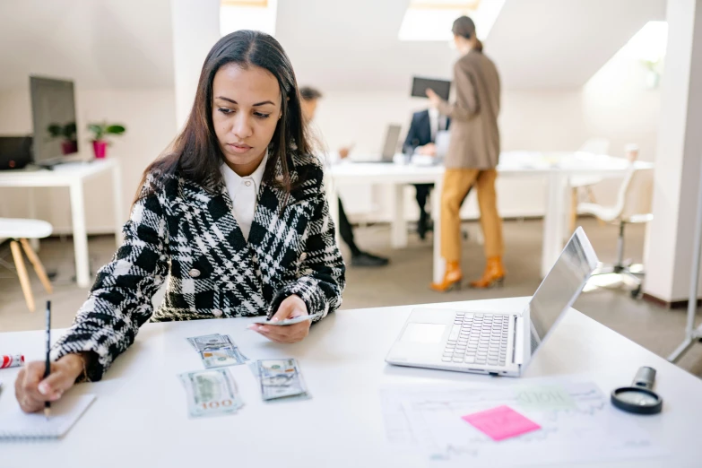 a woman sitting at a table working on a laptop, pexels contest winner, cash on a sidetable, person in foreground, business surrounding, thumbnail