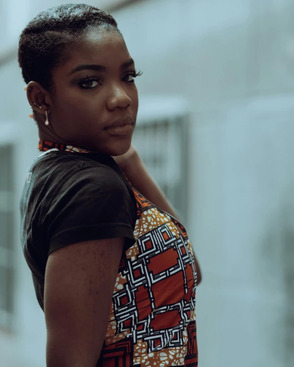 a woman standing in front of a building, by Lily Delissa Joseph, trending on unsplash, afrofuturism, wearing a vest top, low quality photo, thumbnail, traditional clothing