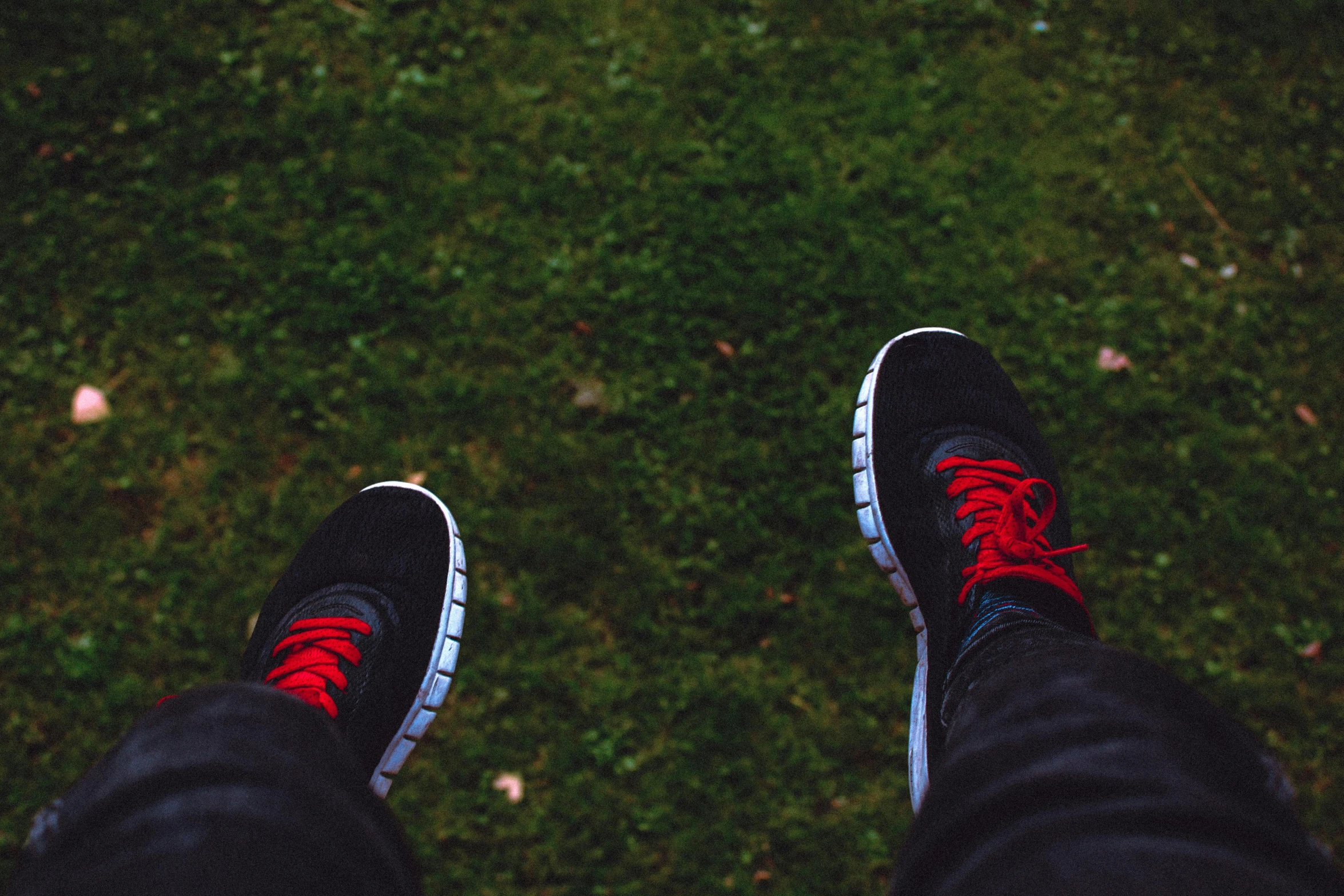 a person standing on top of a lush green field, sneaker, black and red, at a park, waiting