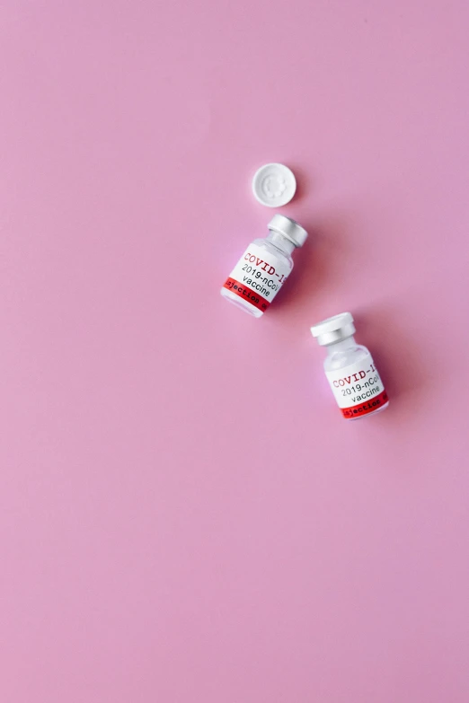 a couple of pills sitting on top of a pink surface, a picture, by Julia Pishtar, trending on pexels, white and red color scheme, vials, cosmopolitan, photo taken with provia