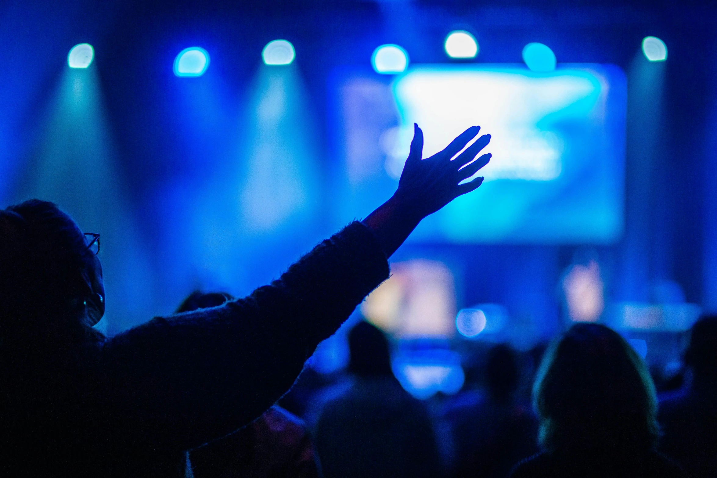 a person raising their hands in front of a stage, pexels, scene from church, blue, instagram post, 15081959 21121991 01012000 4k