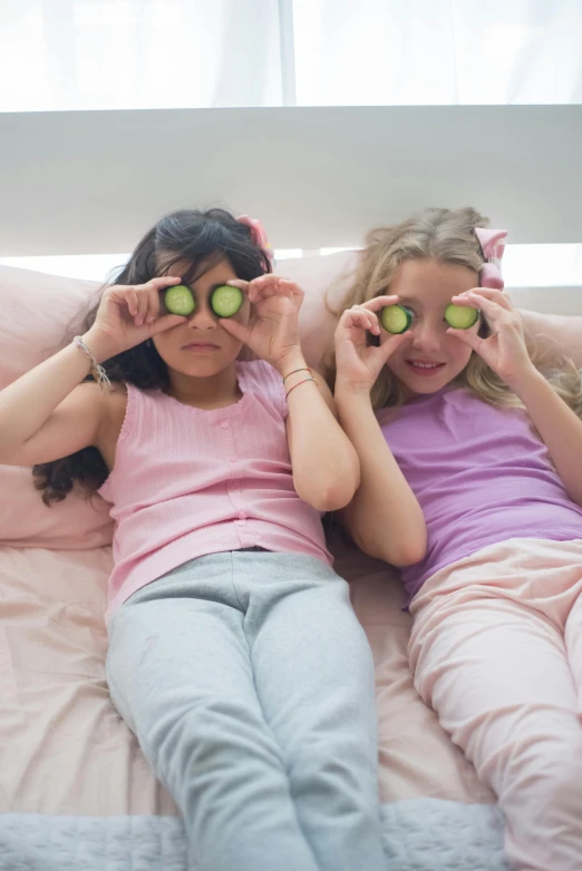 two little girls laying on a bed with cucumbers in their eyes, inspired by Peter Alexander Hay, pexels, teenager hangout spot, medium shot of two characters, ap, fruit