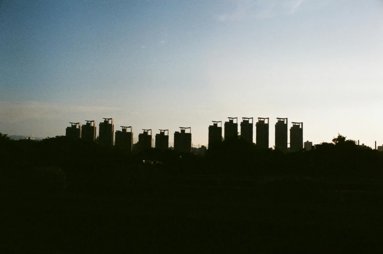 a group of tall buildings sitting next to each other, an album cover, by Attila Meszlenyi, unsplash, brutalism, silhouettes in field behind, 9 steel barrels in a graveyard, golden hour in beijing, photo taken on fujifilm superia