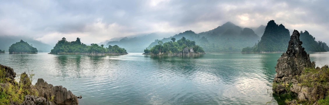 a large body of water surrounded by mountains, an album cover, inspired by Pierre Pellegrini, pexels contest winner, sumatraism, vietnam, light grey mist, islands, lush forests