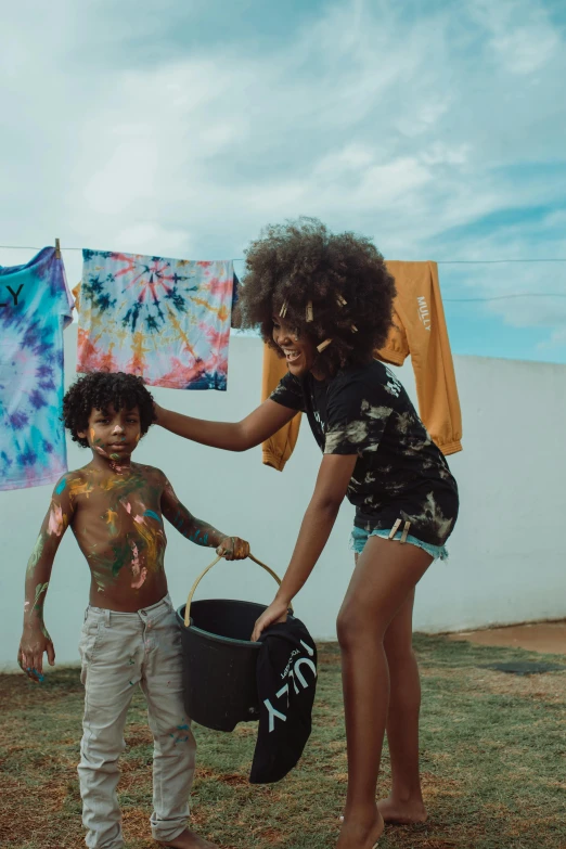 a woman standing next to a boy holding a bucket, pexels contest winner, black arts movement, tie die shirt, brazil, kids playing, long afro hair