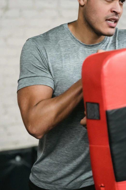 a man standing next to a punching bag, happening, red and grey only, upper body close up, square masculine jaw, local gym