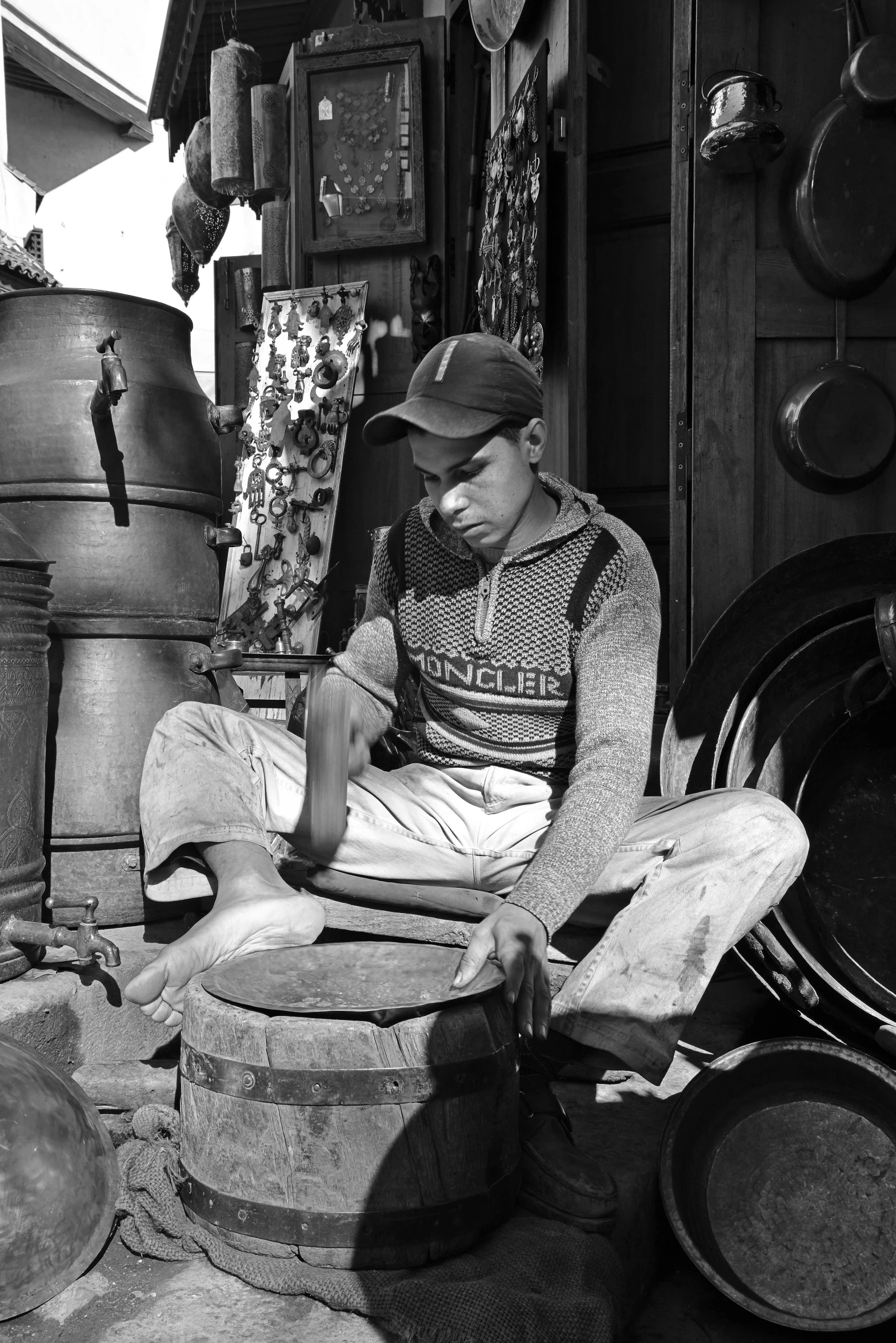 a black and white photo of a man sitting on a barrel, a black and white photo, by Vivian Maier, photorealism, working in the forge, 14 yo berber boy, 15081959 21121991 01012000 4k, medium format. soft light