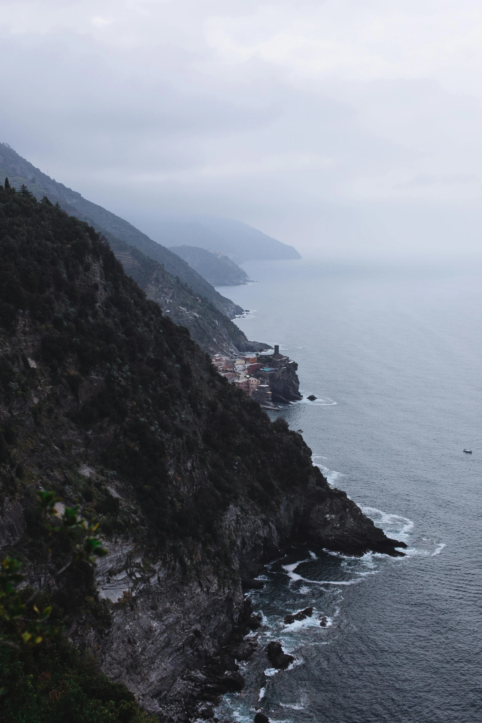 a large body of water next to a lush green hillside, by Carlo Martini, pexels contest winner, cinq terre, under a gray foggy sky, 2 5 6 x 2 5 6 pixels, cliff side at dusk