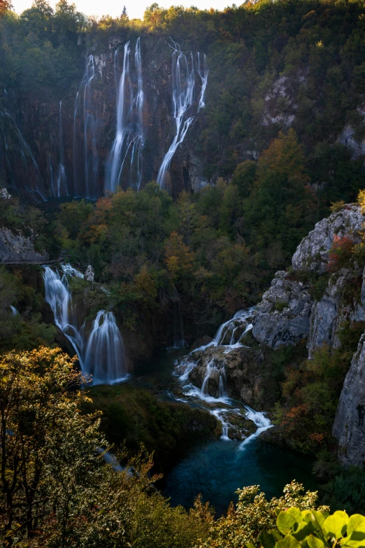 a waterfall in the middle of a lush green forest, by Slava Raškaj, lit in a dawn light, multiple waterfalls, autumnal, croatian coastline