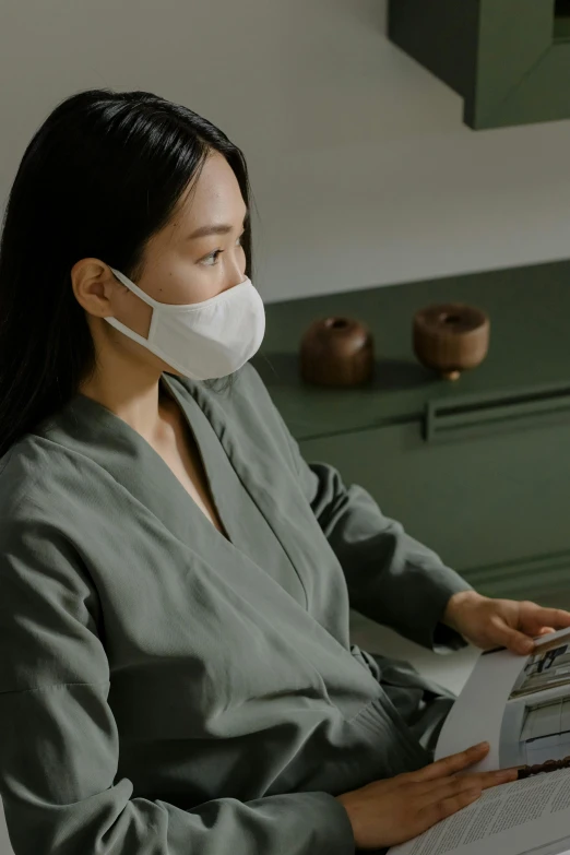 a woman wearing a face mask while reading a book, inspired by Li Di, tech robes, minimalistic aesthetics, on a desk, asia
