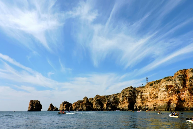 a group of boats floating on top of a body of water, pexels contest winner, romanticism, coastal cliffs, cirrus clouds, portugal, thumbnail