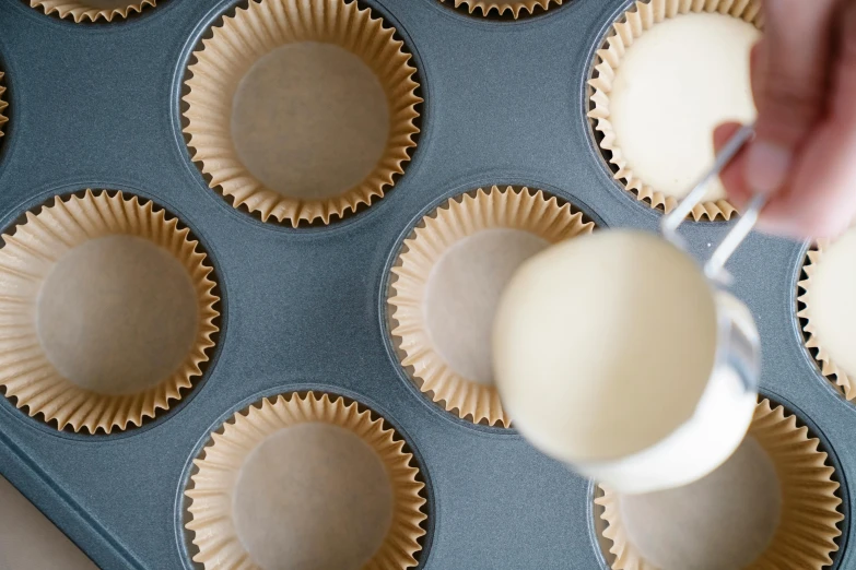 a person pouring batter into a muffin tin, by Sylvia Wishart, trending on unsplash, parchment paper, grey, enamel, fan favorite