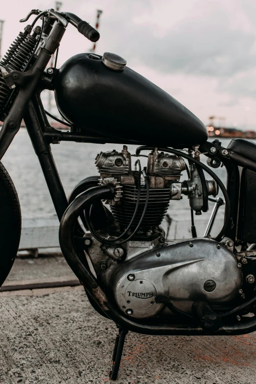 a black motorcycle parked next to a body of water, pexels contest winner, mechanical details, triumph, antique, side view intricate details