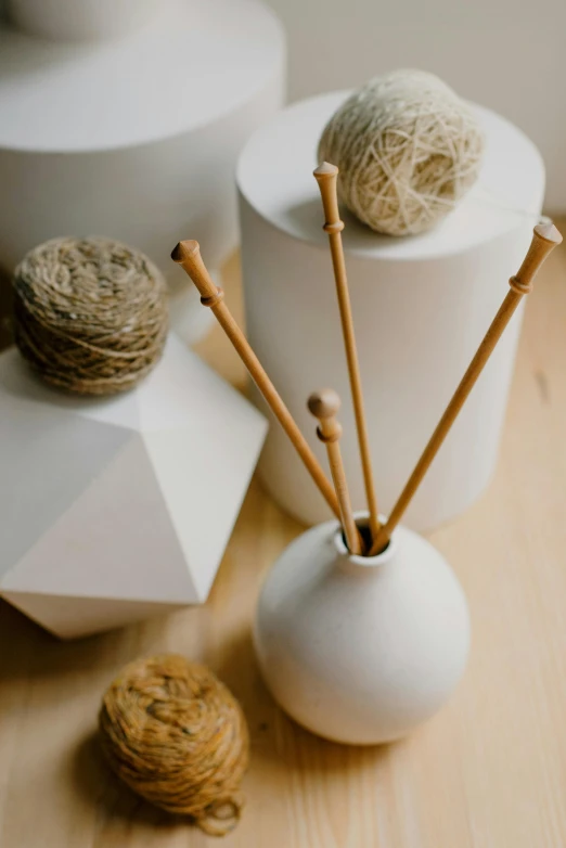 a white vase sitting on top of a wooden table, yarn ball, spines and towers, professional product shot, flax