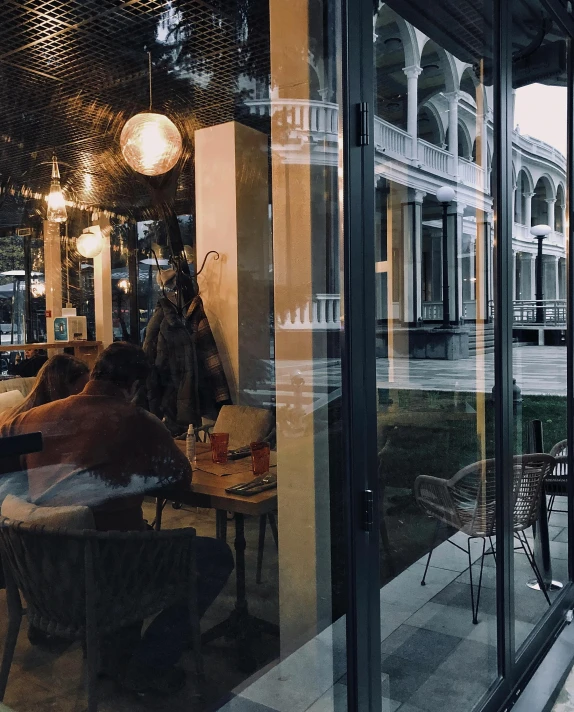 a group of people sitting at a table outside of a restaurant, unsplash contest winner, hyperrealism, clear glass wall, bangkok townsquare, rows of windows lit internally, gif