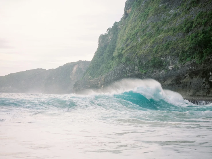 a man riding a wave on top of a surfboard, pexels contest winner, sumatraism, coastal cliffs, teal aesthetic, windy beach, trees and cliffs