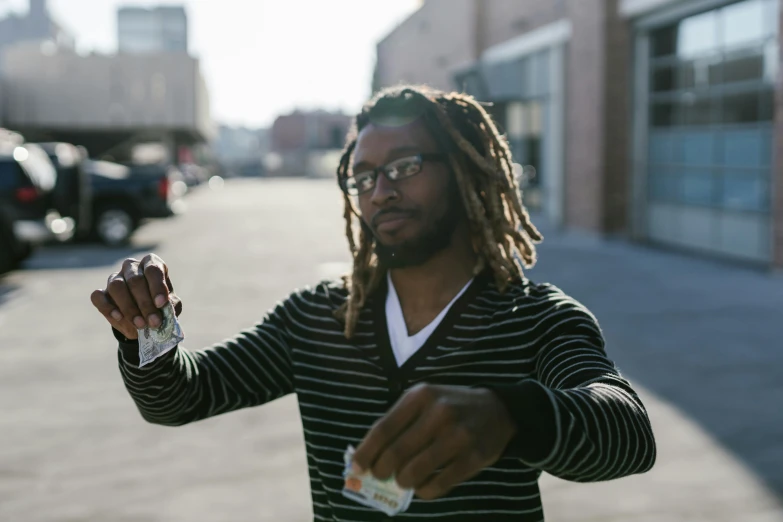 a man with dreadlocks holding something in his hand, a portrait, unsplash, memphis rap, money, person in foreground, slightly sunny