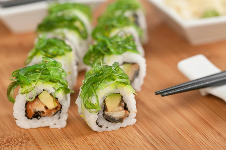 a wooden table topped with sushi rolls and chopsticks, lush greens, looking towards camera, close up image, grey