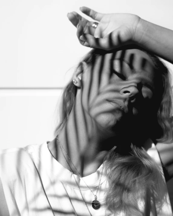 a black and white photo of a woman covering her face with her hands, a black and white photo, unsplash, photorealism, wearing stripe shirt, blonde woman, liquid shadows engulf, hair blowing