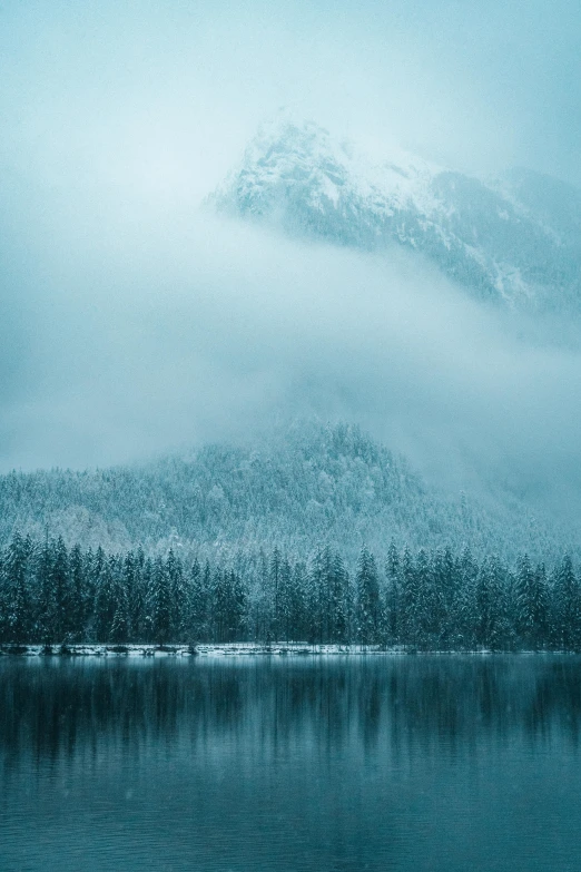 a mountain covered in snow next to a lake, unsplash contest winner, romanticism, cyan fog, fir trees, music, grey