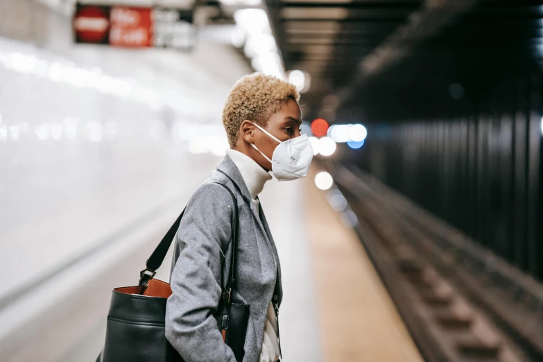 a woman wearing a face mask in a subway station, trending on pexels, afrofuturism, short blonde afro, air pollution, wearing a white lab coat, joel meyerowitz