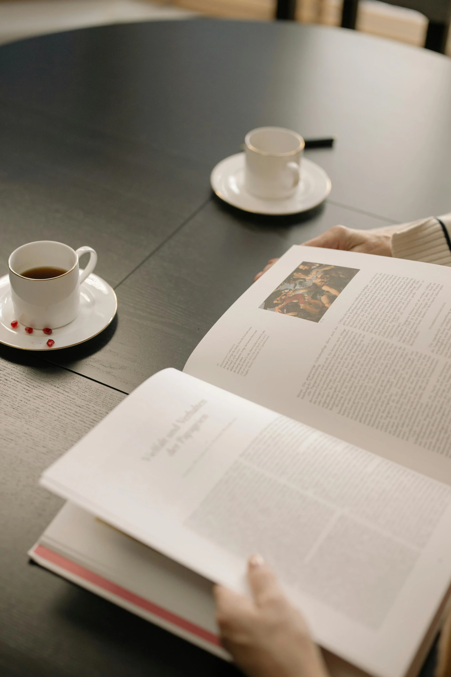 a woman sitting at a table with a book and a cup of coffee, by Matthias Stom, unsplash, hyperrealism, two cups of coffee, print on magazine, in a library, high angle close up shot