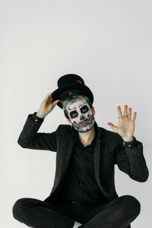 a man in a skeleton mask is sitting on the floor, pexels contest winner, black top hat, set against a white background, facepaint facepaint facepaint, holding his hands up to his face