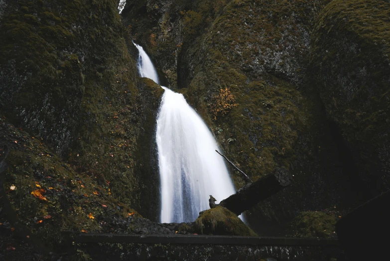 a person standing in front of a waterfall, by Jessie Algie, unsplash contest winner, hurufiyya, near the black cauldron, high angle, fall season, historical photo