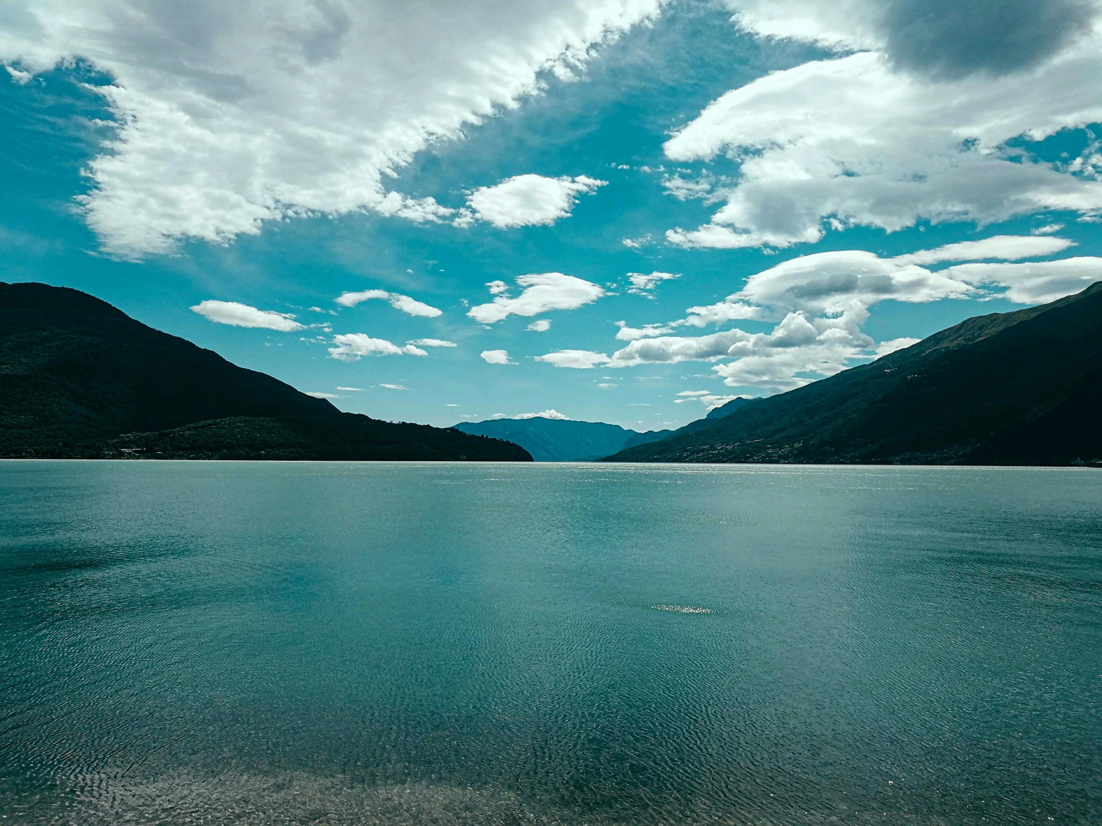 a large body of water with mountains in the background, pexels contest winner, whistler, picton blue, screensaver, peaceful clouds