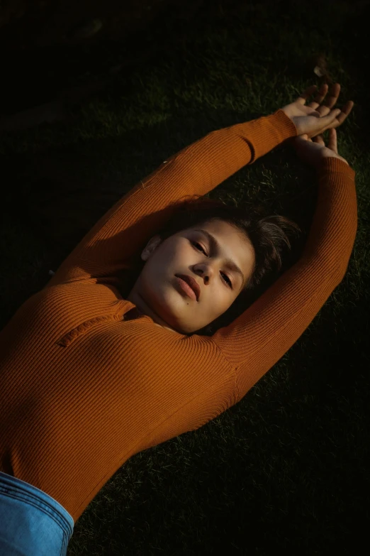 a woman laying on top of a lush green field, an album cover, inspired by Elsa Bleda, trending on pexels, renaissance, orange body, long sleeves, portrait mode photo, dark orange