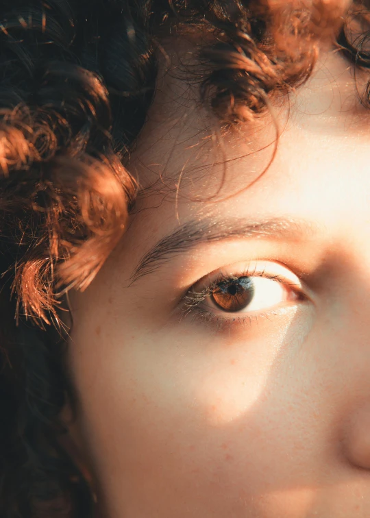 a close up of a person with curly hair, very bright brown eyes, directional sunlight skewed shot, light-brown skin, trustworthy eyes