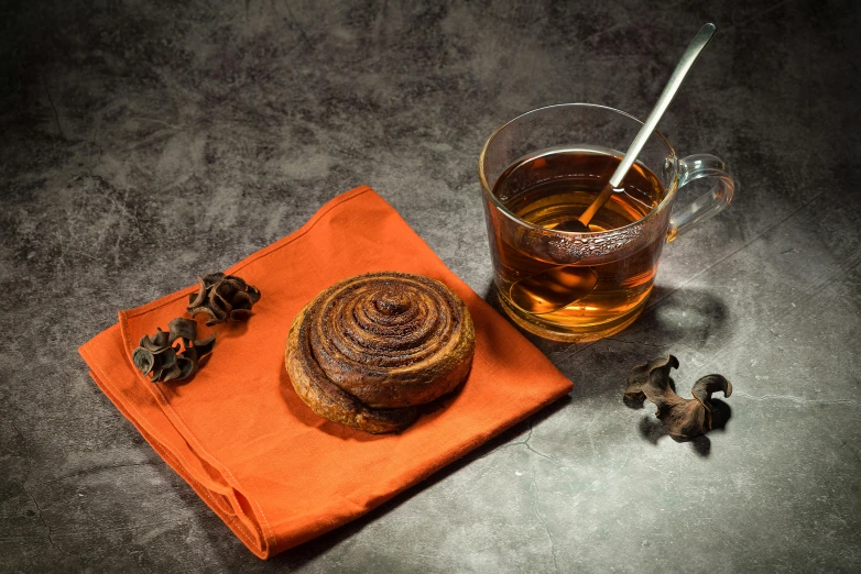 a cup of tea and a cinnamon roll on a napkin, inspired by Charles Le Roux, hurufiyya, dark orange, chocolate frosting, thumbnail, mead