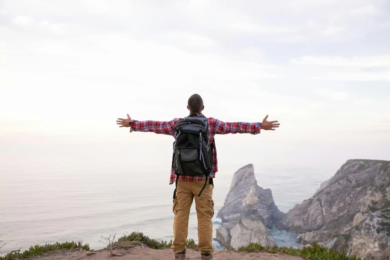 a man standing on top of a mountain with his arms outstretched, pexels contest winner, with a backpack, avatar image, ocean view, casually dressed