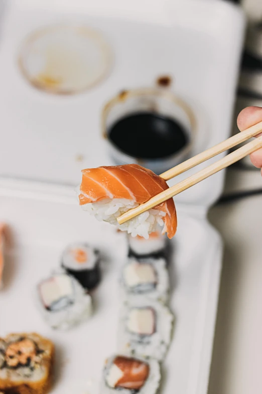 a person holding chopsticks over a tray of sushi, unsplash, 2000s photo, epicurious, salmon, tsunami