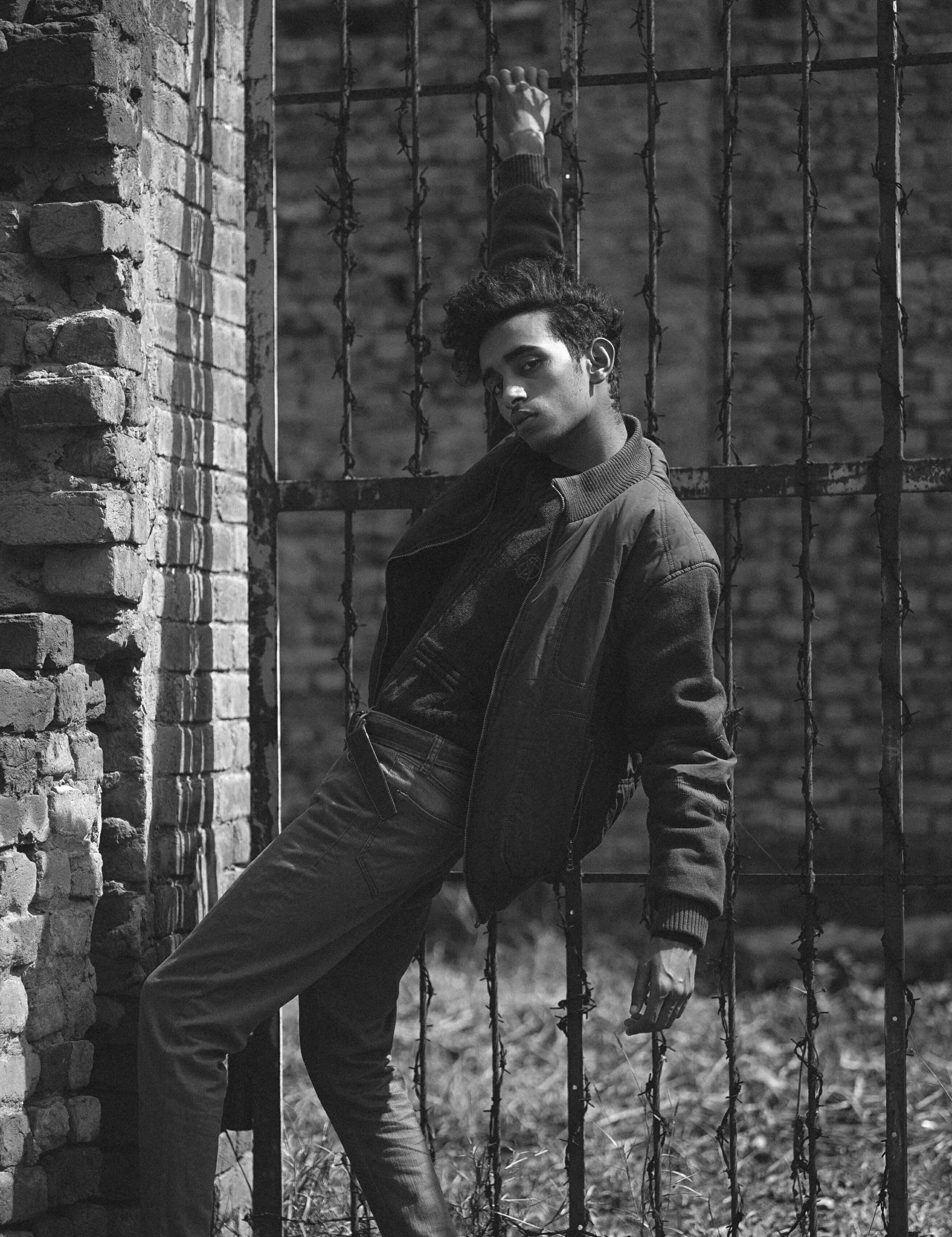 a black and white photo of a man leaning against a fence, androgynous male, in style of stanislav vovchuk, avan jogia angel, 1990 photograph