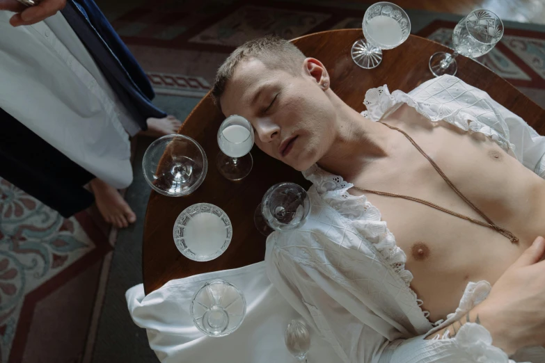 a man in a wedding dress laying on a table, inspired by Konstantin Somov, tumblr, renaissance, cups and balls, margiela campaign, in a movie still cinematic, thin young male alchemist