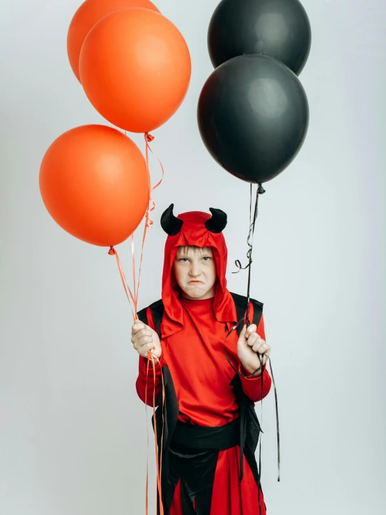 a little girl dressed in a devil costume holding balloons, by Julia Pishtar, pexels contest winner, teenage boy, plain background, 7 0 years old, black horns