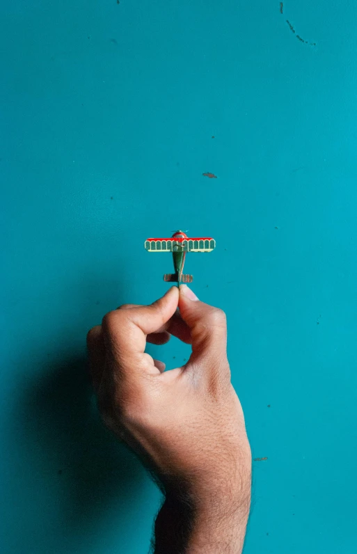 a person holding a toothbrush in front of a blue wall, an album cover, pexels contest winner, conceptual art, dragonfly-shaped, red and teal color scheme, view from above, paper airplane