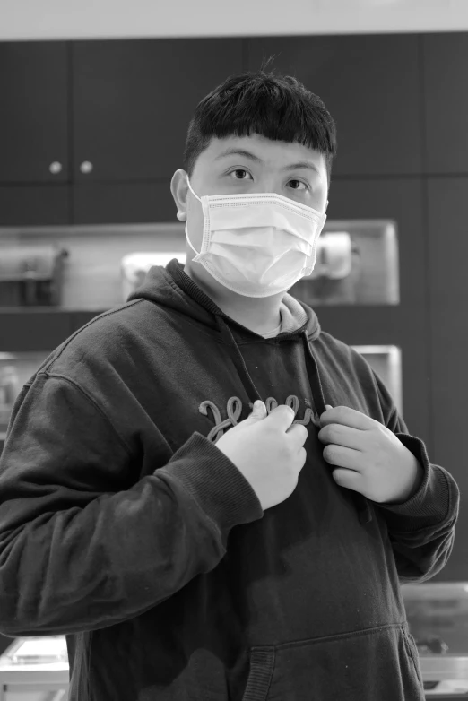 a man wearing a face mask in a kitchen, an album cover, inspired by Weiwei, pexels contest winner, hyperrealism, portrait of 14 years old boy, monochrome:-2, appearing in a shopping mall, chest coverd