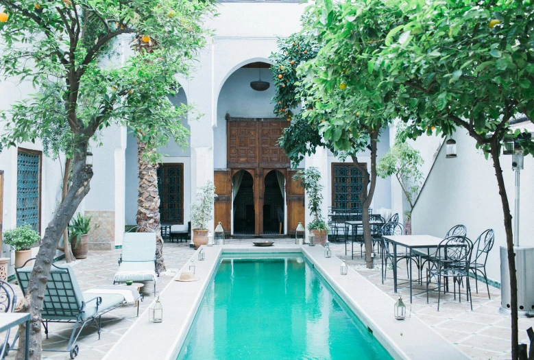 a pool in the middle of a courtyard with tables and chairs, inspired by Riad Beyrouti, trending on unsplash, arabesque, exotic trees, conde nast traveler photo, exterior, thumbnail