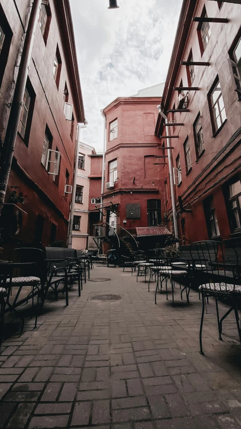 a couple of benches sitting next to each other on a sidewalk, by Cafer Bater, pexels contest winner, art nouveau, soviet yard, red building, tables and chairs, standing in an alleyway