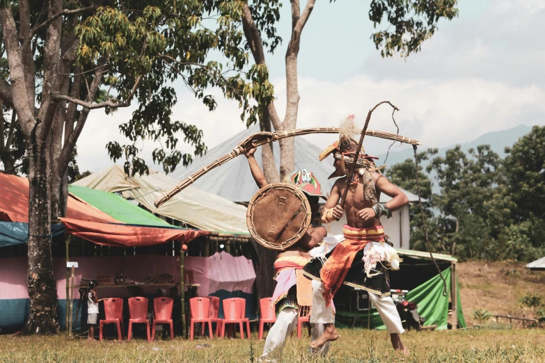 a couple of people that are standing in the grass, hurufiyya, tribal dance, kuntilanak on tree, with bow and arrow, festival vibes